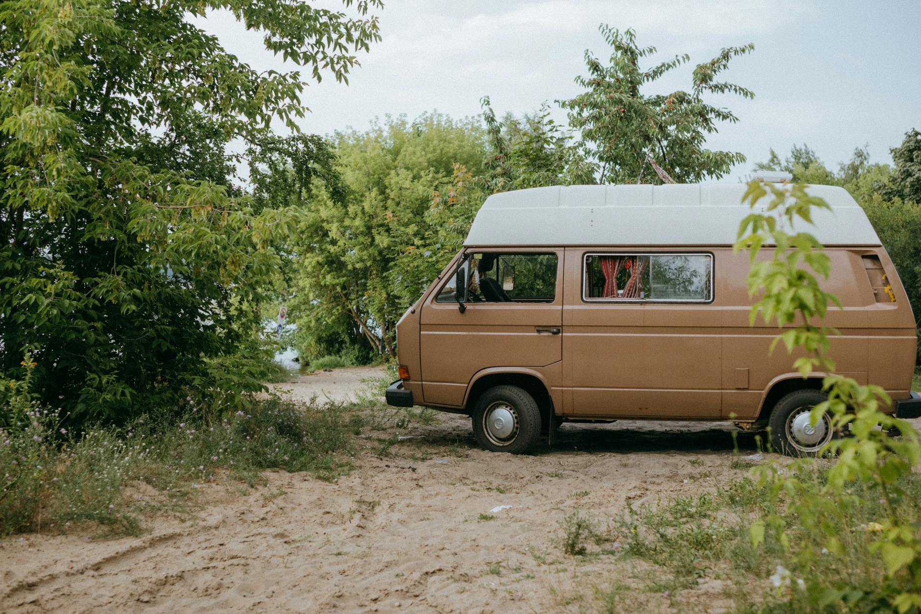 Brązowy kamper zaparkowany na piasku wśród zielonych drzew