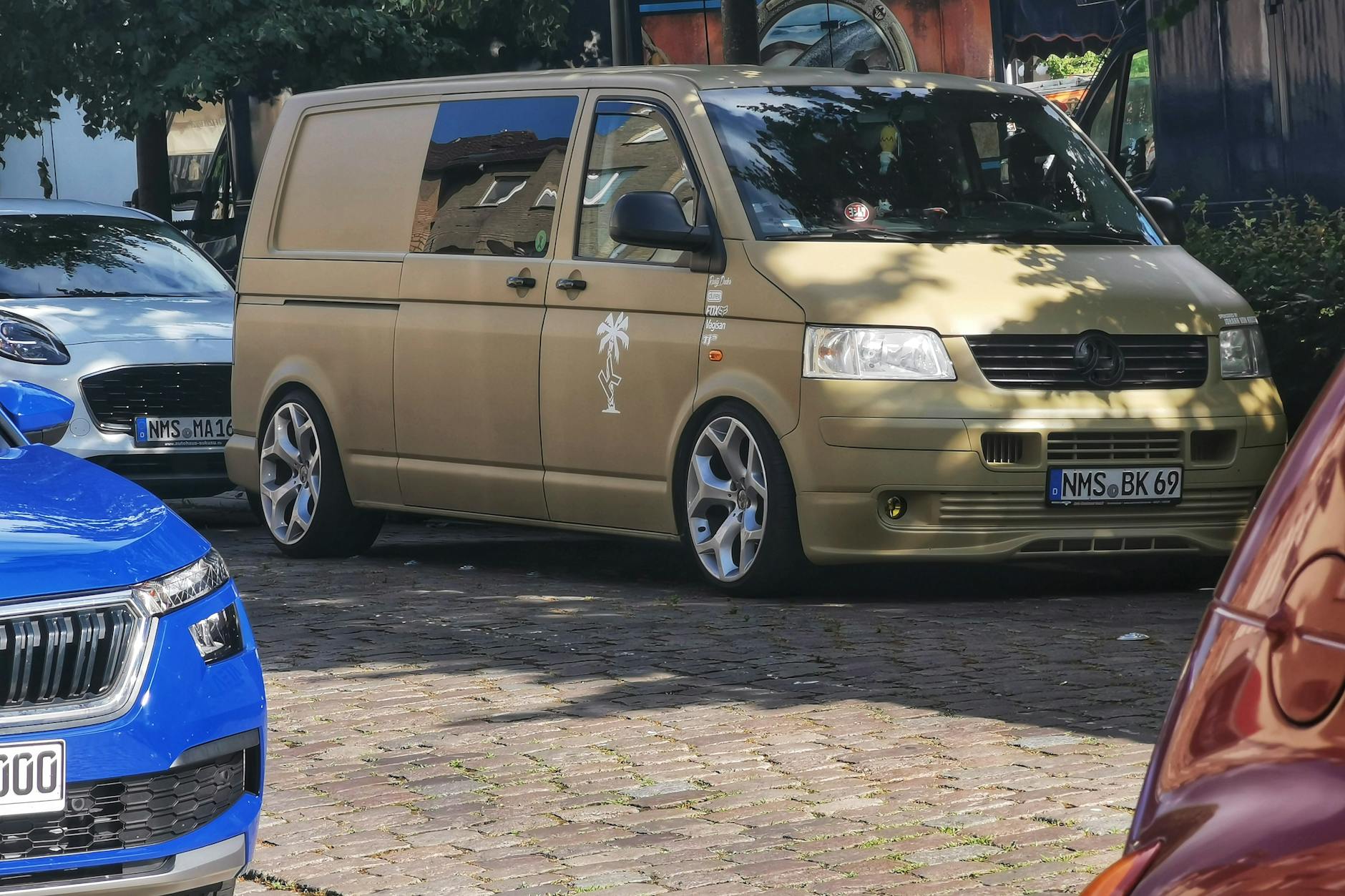 Kamper zaparkowany między samochodami na brukowanej ulicy w cieniu drzew