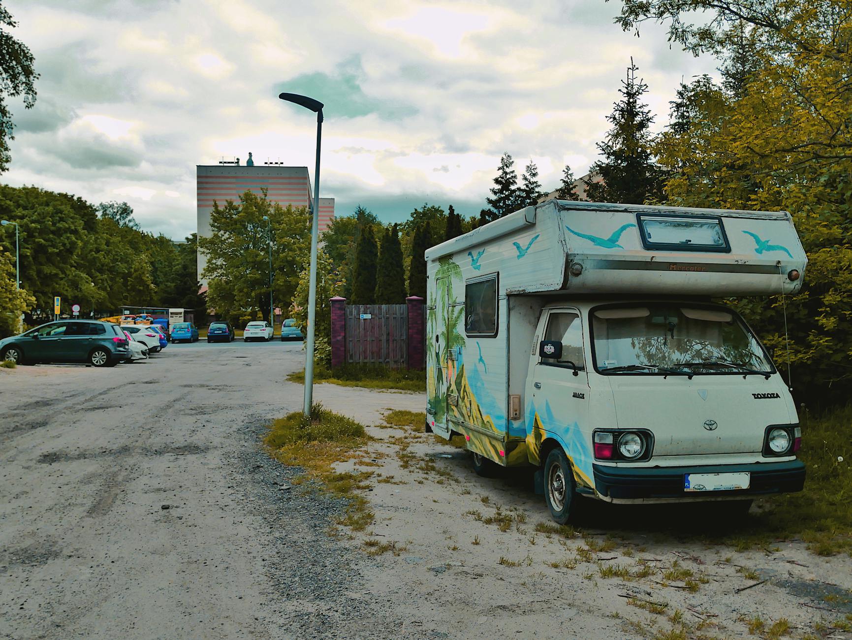 Kolorowy zabytkowy kamper zaparkowany przy ulicy wśród drzew i kamienic