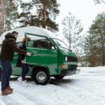 Para przy klasycznym zielonym kamperze na zimowym postoju w lesie